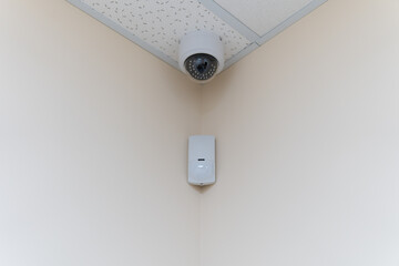 Security camera and motion detector installed on ceiling in room.