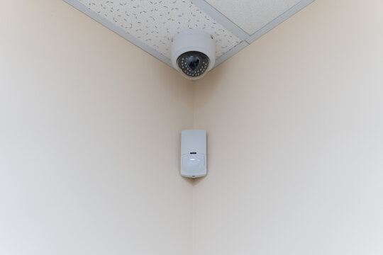 Security camera and motion detector installed on ceiling in room.