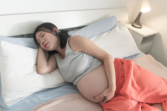 home portrait of young tired and depressed Asian Chinese woman pregnant in bed having nausea and feeling unwell suffering pregnancy body pain and fatigue