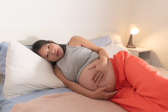 lifestyle home portrait of young happy and beautiful Asian Japanese woman pregnant lying relaxed on bed excited about maternity touching her belly in pregnancy concept