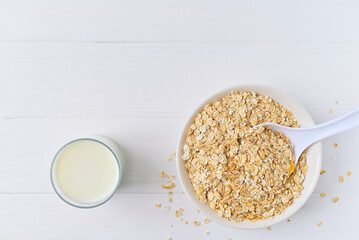 bowl of granola with a spoon and a glass of oat milk. white wooden background. top view. copy space.