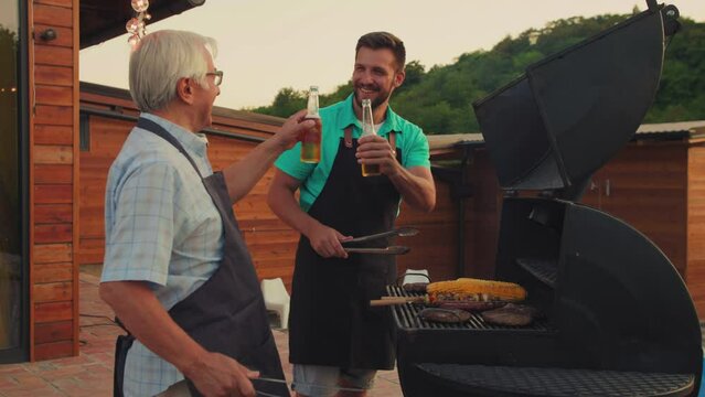Two smiling men (young and old) drinking beer in the summer garden while b