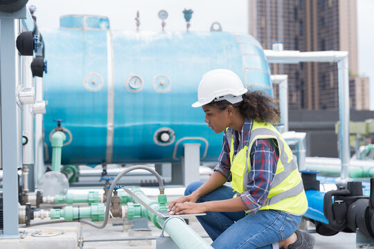 Female engineer working with laptop computer for maintenance in sewer pipes area at construction site. African American woman engineer working in workplace at rooftop of building