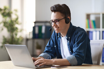 Fototapeta premium Telecommuting Concept. Young Male Manager In Headset Working With Laptop In Office
