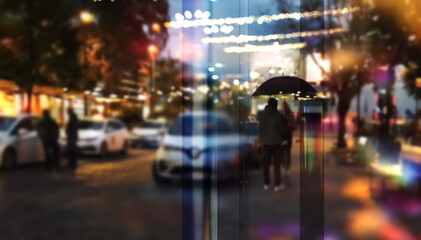 Fototapeta na wymiar city night light view from windows glass on street , people walk with umbrella cold rainy season Autumn background urban scene