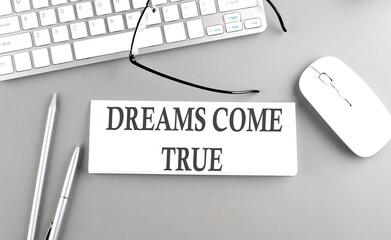 DREAMS COME TRUE text on paper with keyboard on grey background