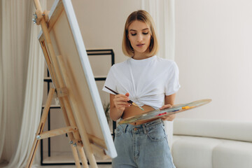 The artist paints in the studio. Attractive girl wearing a white T-shirt