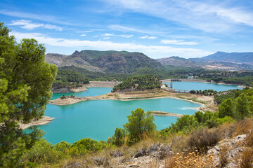 Fototapeta na wymiar Spectacular panoramic views of the Guadalhorce reservoir, next to the Caminito del Rey in Malaga, Spain. Turquoise blue water and forest with blue sky on a sunny day.