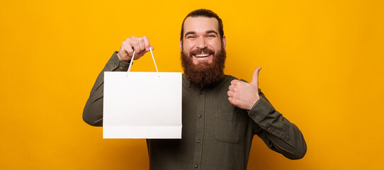 Ecstatic man recommends the offer while holding a shopping bag with copy space.