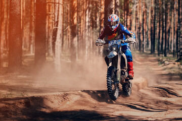 motorcycle racer on an enduro sports motorcycle rides fast on a dusty road in the forest in an...