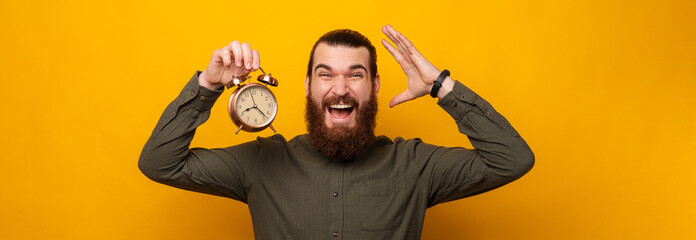 Bearded man is mad because time flys so fast while holding an alarm clock.