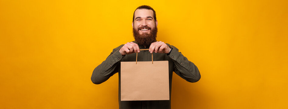 Excited man is showing to the camera a craft shopping bag with copy space.