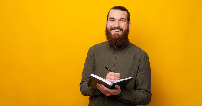 Content bearded man smiles at the camera while holding a planner and a pen.