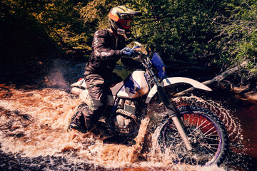 motorcycle racer on an enduro sports motorcycle crosses a river in a ford in an off-road race in...