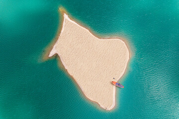 Small uninhabited, desert sand island in the middle of sea with sup board. Drone view, aerial view,...
