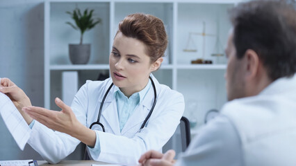 doctor in white coat pointing with hand at cardiogram and talking to patient in clinic.