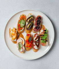 Brushetta, antipasti  or authentic traditional spanish tapas set on white plate. Variety of  pinchos (pintxos) in a bar or restaurant or home party or picnic. Flat lay, top view