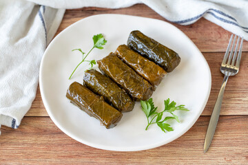 Wrapped leaves with olive oil on a wooden background. Traditional Mediterranean cuisine delicacies. Local name zeytinyagli yaprak sarma or dolmadika. close up