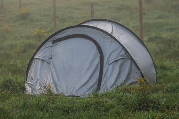 Simple grey foldable tent in a green field with water beads on the grass. Travel and outdoor activity. Holiday in nature.