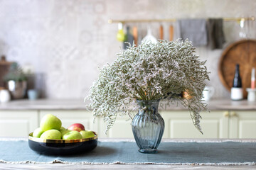 Bowl of fresh apples and glass vase with bouquet of flowers on kitchen counter. Space for text. Clean kitchen with minimal style decoration. Bouquet of dry flowers at home	