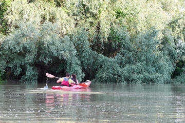 They love kayaking together. Confident young couple kayaking on summer river together near green trees