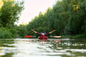 A woman lies in a kayak waving her arms like a butterfly at summer river. Splashing water and hands like butterfly wings