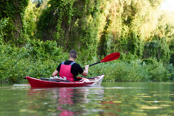 Man in red kayak in red life jacket kayaking in wild Danube river on biosphere reserve in spring