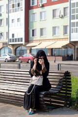 A Muslim woman is resting a bench in the park, tidying herself up by looking in a mirror.