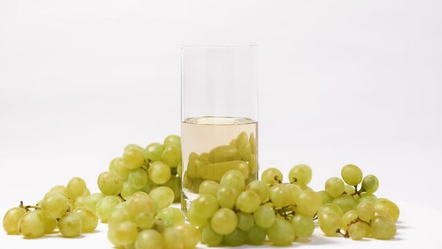Glass of grape juice and bunches of green grapes. Filling glass with grape juice. Stop motion. Rotation
