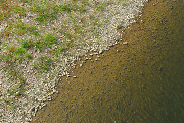 Rocky shore with grass top view. Round stones and clear wate. River bank, view from above
