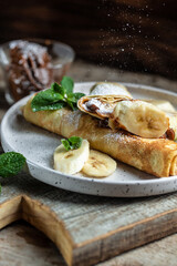 Crepes stuffed with chocolate spread and banana on white plate. Thin pancakes, blini. Delicious breakfast or snack. Food recipe background. Close up