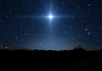 Bright star, starry sky and forest silhouette. Star indicates the Nativity of Jesus Christ in the...