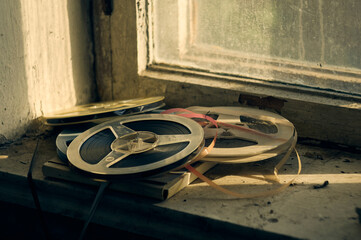 Reels of magnetic film for a reel-to-reel tape recorder lie on the windowsill, an old abandoned...