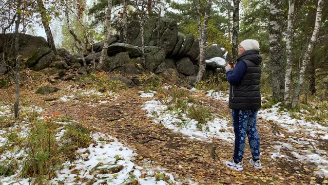 A woman walks in the autumn forest in bad weather and takes pictures on her smartphone.