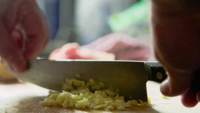 man is preparing dinner by cutting garlic and onions on the kitchen table. close up shot of knife dicing the delicious food to small pieces to add to tonight meal