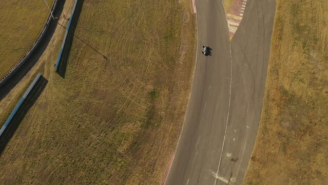 A dynamic tilting aerial shot while tracking a running race car passing below the drone. This is the Aut&oacute;dromo de Buenos Aires Oscar y Juan G&aacute;lvez motor racing circuit in Buenos Aires, Argentina.
