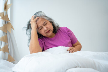 Unhealthy elderly senior Asian woman sitting on bed suffering from headache and migraine so pain and illness, Stress senior woman sit on bed at home alone, tried, Unhappy Elderly despond concept