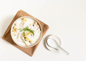Cold soup with kefir okroshka in a white bowl on a brown napkin on a white background. View from above.