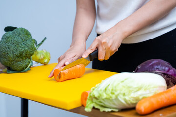 Young woman cutting vegetables in the kitchen. Woman's hands cutting vegetables, behind fresh vegetables. asian woman uses a knife and cooks.