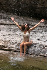 Fototapeta na wymiar Young beautiful woman splashing water in a river sitting on some rocks