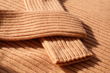 Fototapeta na wymiar Biege knitted textile jumper with sleeves, sunlight, close-up