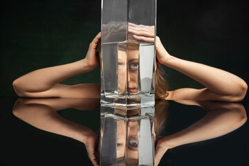 Surreal art photography. Young girl's face through glass vase over dark green background. Object...
