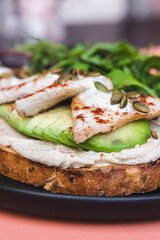 Bruschetta with pate, avocado and herbs sprinkled with sunflower seeds on a pink background
