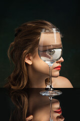 Creative art photography. Closeup girl's face through wine glass over dark background. Object...