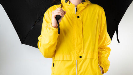 A woman in a yellow raincoat holds a black umbrella on a white background
