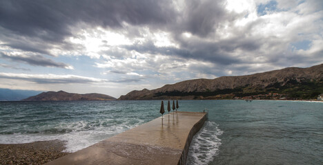 Beach of Baska, Krk, Croatia, on a cloudy day with dramatic sky, waves and mountains (Panorama) 
