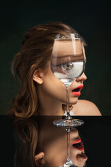 Creative art photography. Stylish girl's face through wine glass over dark green background. Object distortion, optical illusion. Minimalistic contemporary art.