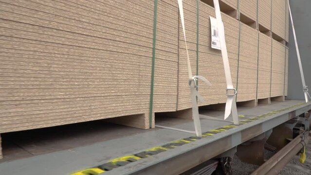 A large stack of full size OSB chipboard on a pallet strapped into a train car for transportation, hd