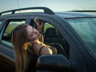 Fototapeta na wymiar Girl sticking her body out of a car window at sunset/ road trip