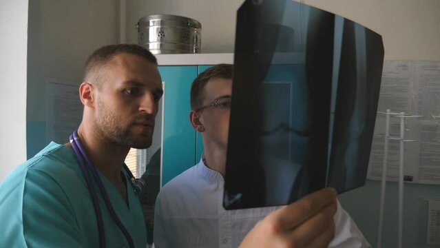 Medical workers in hospital examine x-ray prints. Two caucasian doctors view mri picture and discussing about it. Male medics consult with each other while looking at x ray image. Close up